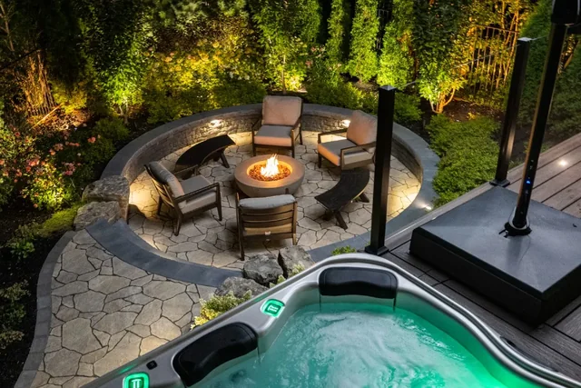 A fire pit, hot tub and landscape lighting in a finished backyard at night.