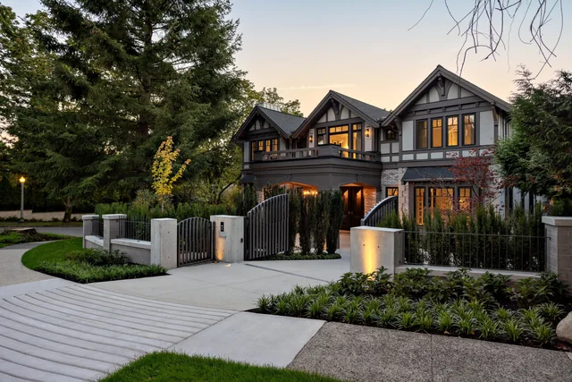A paved entrance court with gates and landscape lighting at dusk.